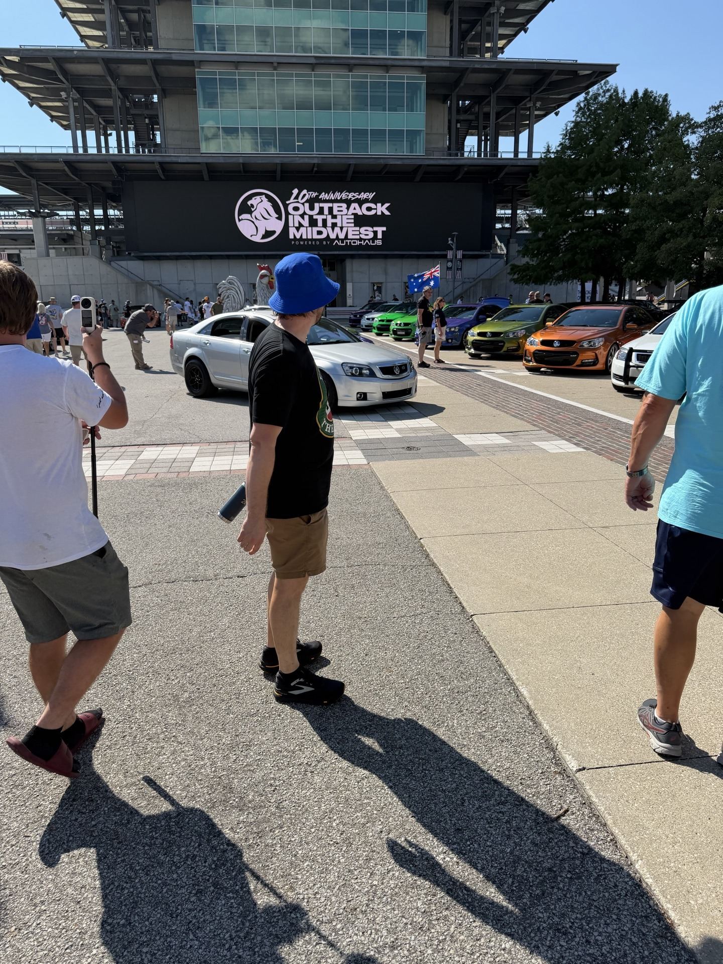 Row of colorful cars in front of the IMS video screen displaying the Outback in the Midwest logo